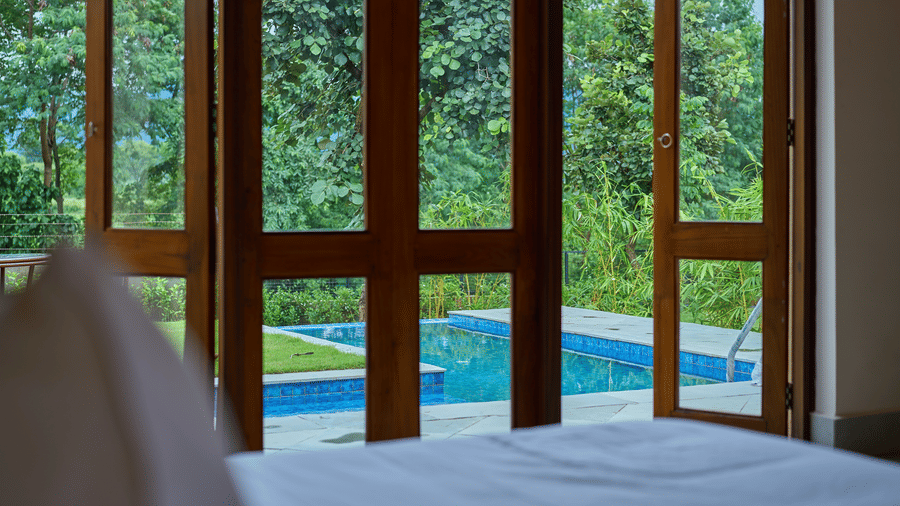 A bedroom featuring open wooden glass doors looking out onto a private swimming pool at Hotel Sonar Bangla, Ajodhya Hills.