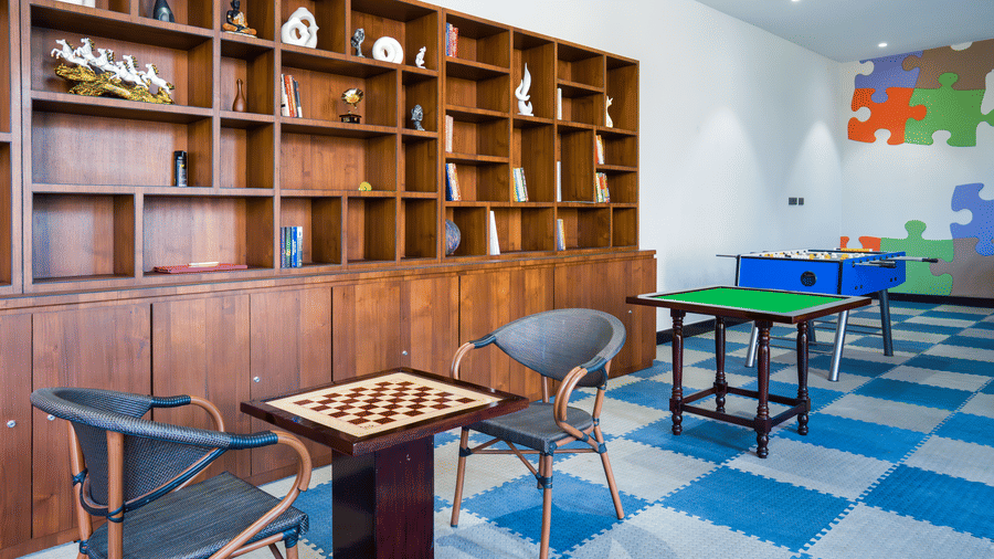 An indoor room featuring a large wooden bookshelf, a chessboard table, and game tables on a checkered floor at Hotel Sonar Bangla, Ajodhya Hills.