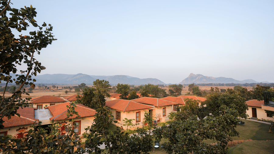 An elevated daytime view featuring cottages with terracotta roofs surrounded by trees and distant hills at Hotel Sonar Bangla, Ajodhya Hills.