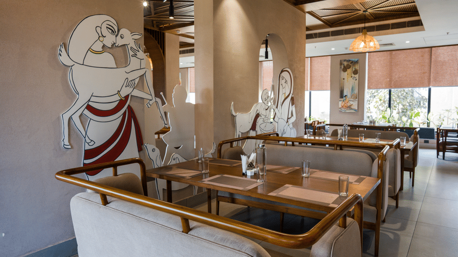 A dining area featuring tables, cushioned benches and painted artwork on pillars at Hotel Sonar Bangla, Ajodhya Hills.