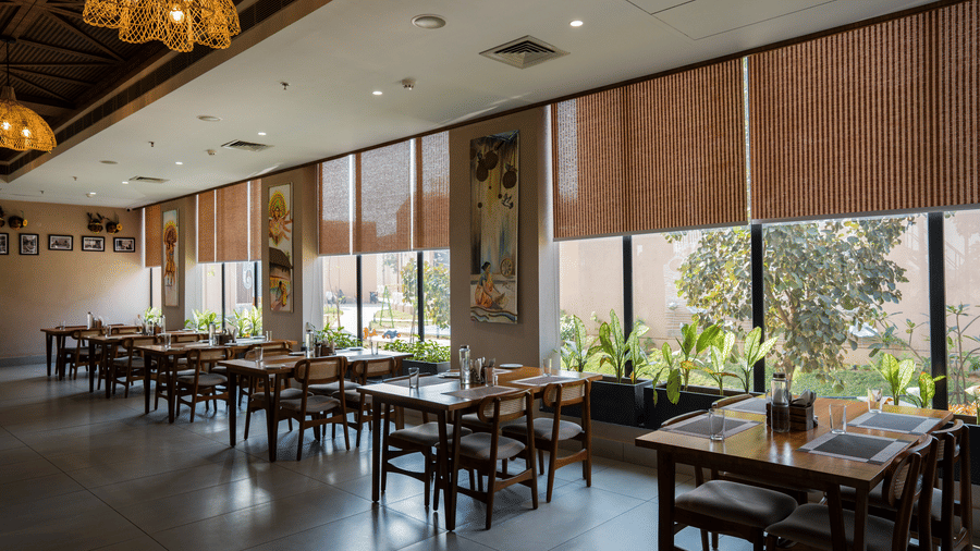 A dining room featuring rows of wooden tables next to large windows at Hotel Sonar Bangla, Ajodhya Hills