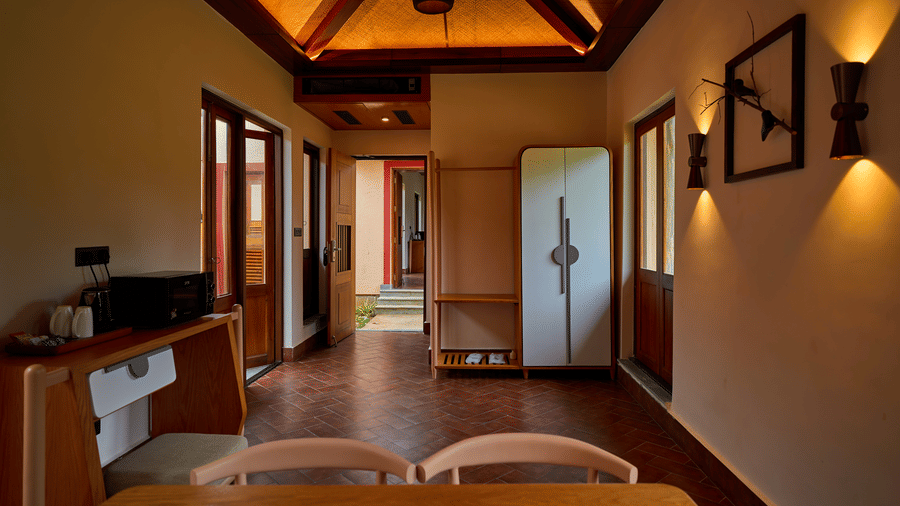 A room interior featuring a dining table, a wardrobe, and terracotta flooring under warm lighting at Hotel Sonar Bangla, Ajodhya Hills.