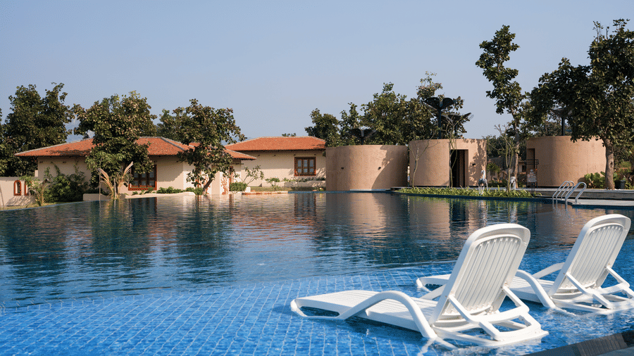 A swimming pool featuring 2 white lounge chairs partially submerged in the shallow end at Hotel Sonar Bangla, Ajodhya Hills.