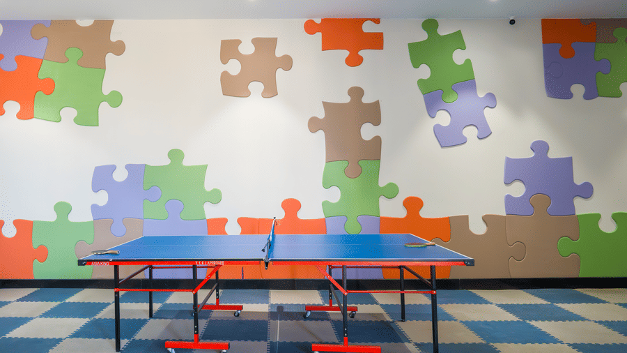 An indoor game room featuring a blue table tennis table and a wall decorated with colourful puzzle pieces at Hotel Sonar Bangla, Ajodhya Hills.