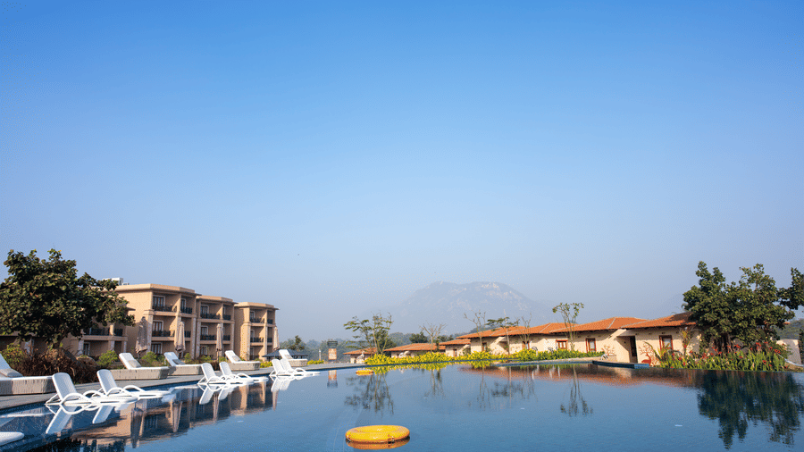 A wide exterior view featuring a large swimming pool with calm water reflecting the surrounding buildings at Hotel Sonar Bangla, Ajodhya Hills.