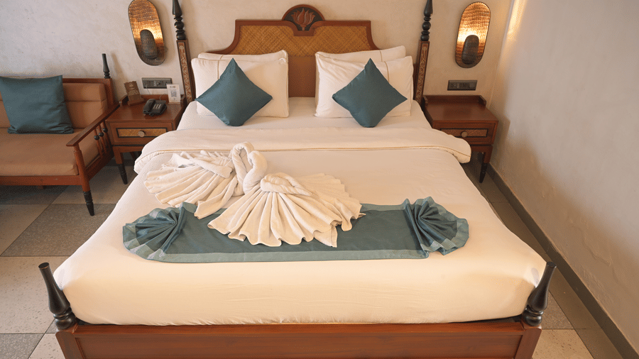  A double bed with white linen and teal accents featuring decorative towel art on the duvet at Hotel Sonar Bangla, Mayapur.
