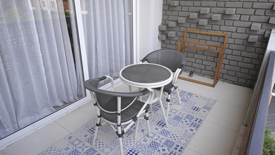 A balcony with patterned floor tiles featuring 2 grey chairs and a small white round table at Hotel Sonar Bangla, Mayapur.