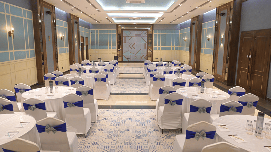 A straight, centred view of the banquet hall with round tables and chairs at Hotel Sonar Bangla, Mayapur.