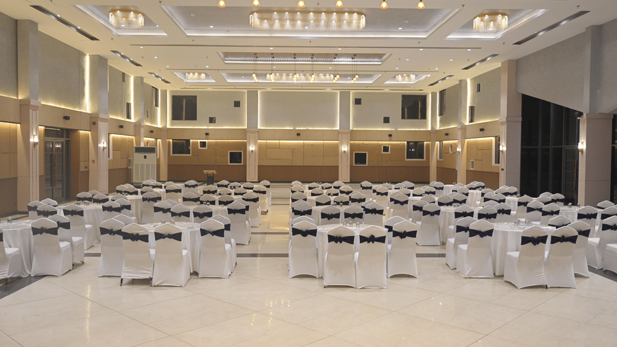 A wide view of a bright banquet hall arranged with rows of chairs accented with sashes at Hotel Sonar Bangla, Mayapur.