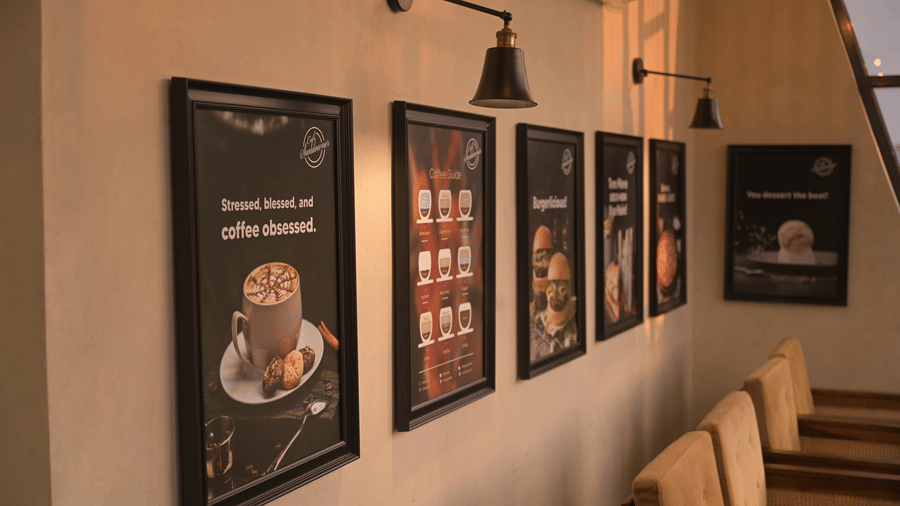 Framed coffee-themed artwork displayed along a softly lit wall inside the cafe at Hotel Sonar Bangla, Mayapur.