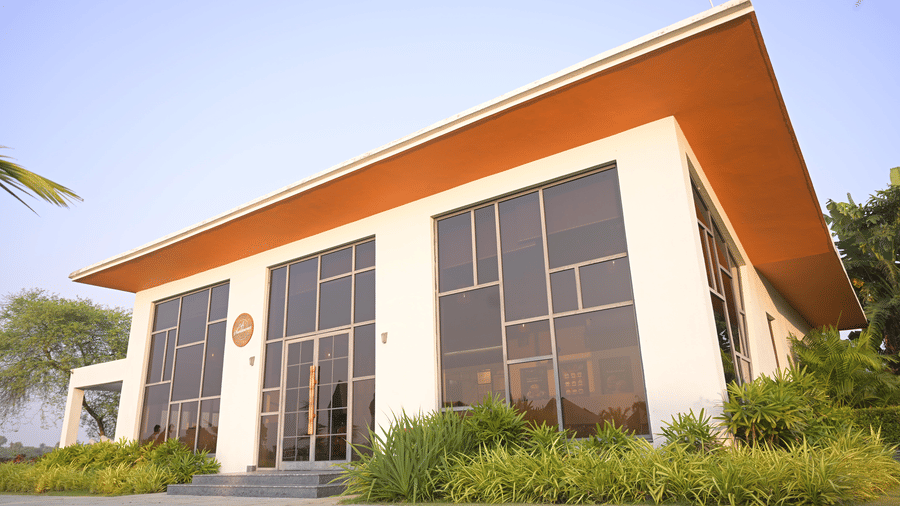 A cafe building with tall glass windows, a slanted roof, and surrounding greenery at Hotel Sonar Bangla, Mayapur.