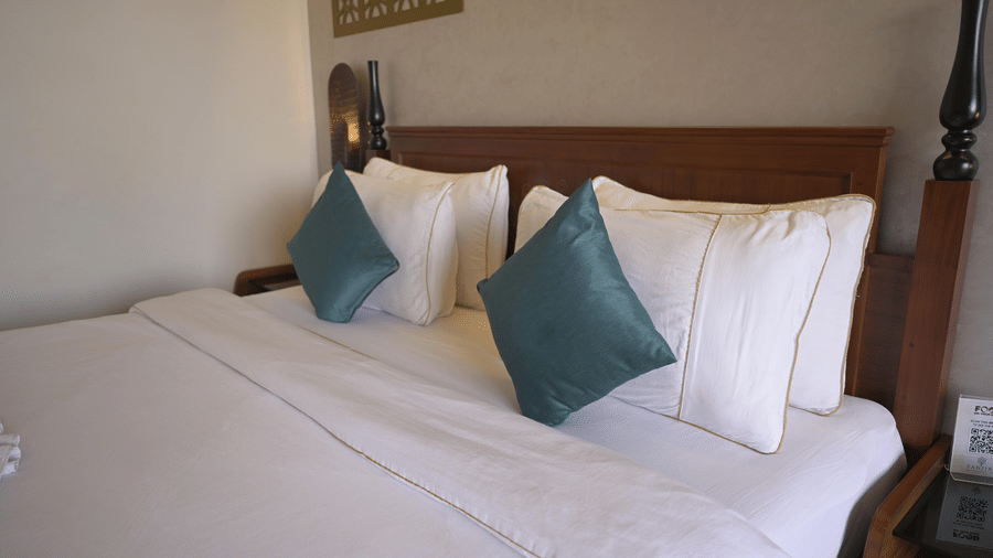 A side view of a double bed with a wooden headboard and teal accent pillows at Hotel Sonar Bangla, Mayapur.