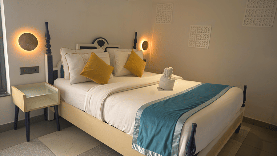 A bed with illuminated circular wall lamps on either side and a blue bed runner at Hotel Sonar Bangla, Mayapur.
