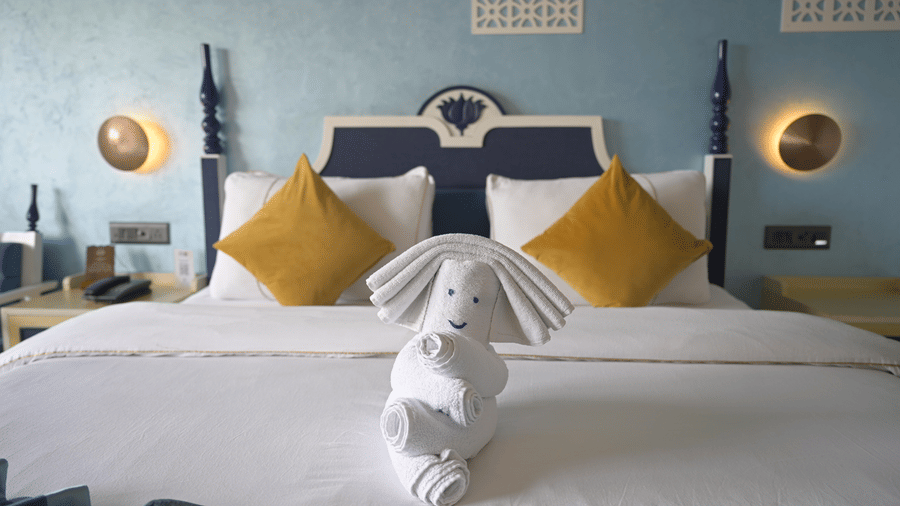  A close up of a bed with yellow pillows and a towel folded into a figure at Hotel Sonar Bangla, Mayapur.