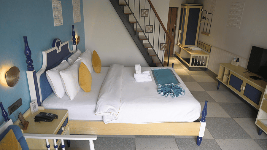 A high-angle view of a guest room showing the bed, television console, and stairs at Hotel Sonar Bangla, Mayapur.