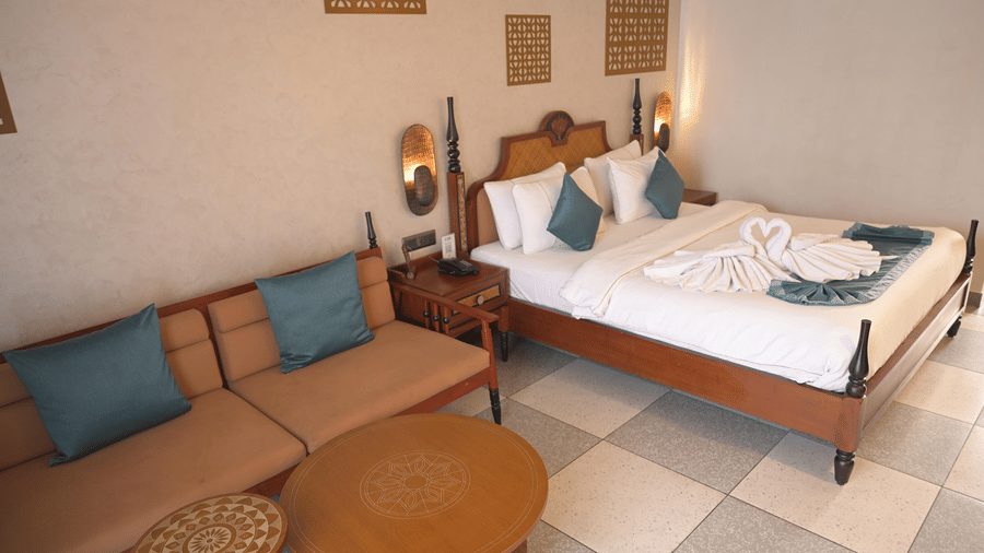 A guest room featuring a sofa, coffee tables, and a double bed with blue accents at Hotel Sonar Bangla, Mayapur.