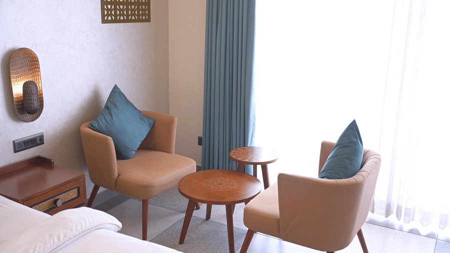 2 tan armchairs with blue cushions and small wooden coffee tables in a guest room at Hotel Sonar Bangla, Mayapur.
