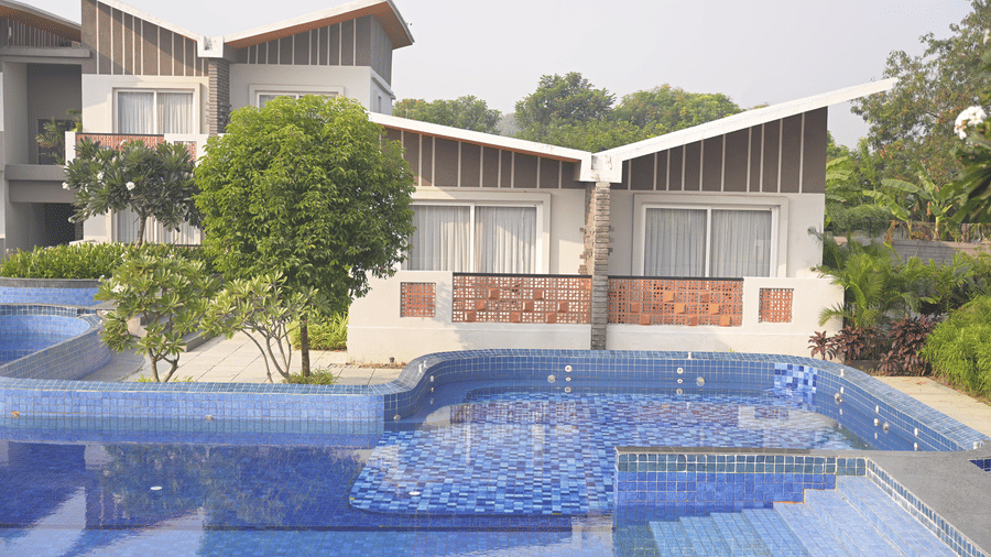 Modern hotel villas with white walls and slanted roofs situated behind a blue swimming pool at Hotel Sonar Bangla, Mayapur.