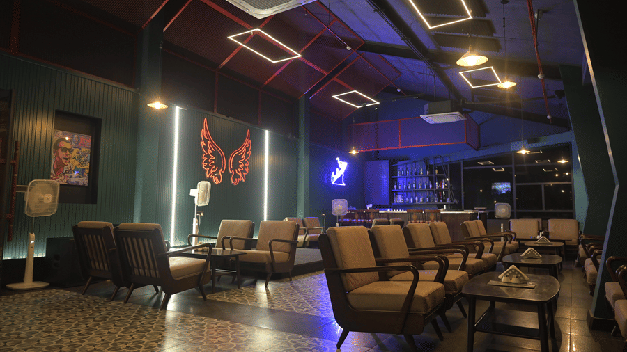 A lounge setting featuring cushioned chairs and a neon butterfly wall installation glowing in the background at Hotel Sonar Bangla, Mayapur.