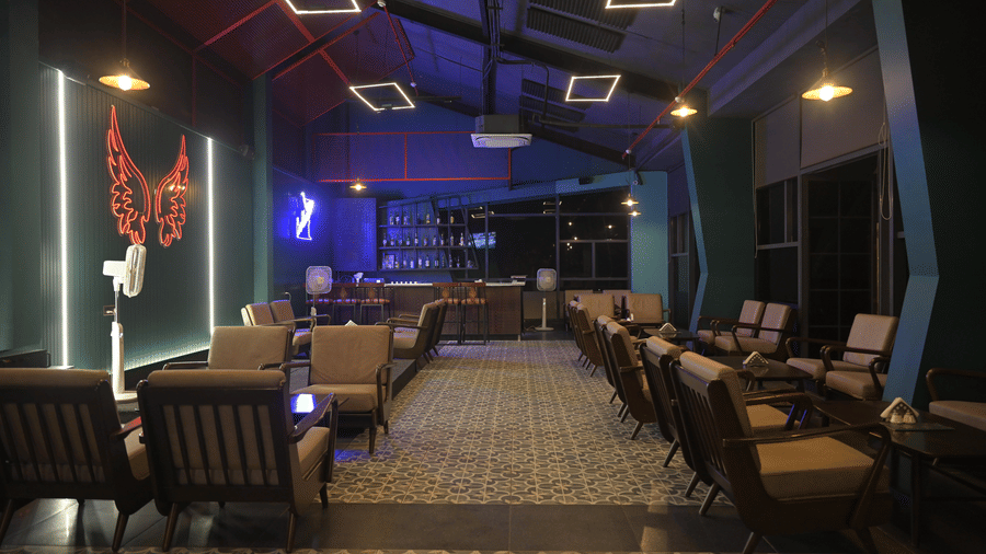 A wide evening view of the lounge bar with warm seating, patterned flooring, and soft neon lighting at Hotel Sonar Bangla Mayapur.