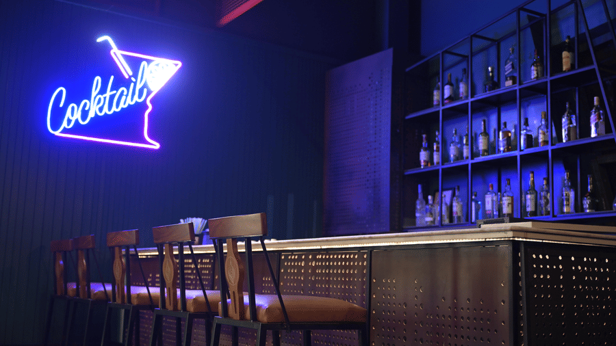 A neon-lit cocktail bar with high stools and a blue glow highlighting the drinks display at Hotel Sonar Bangla, Mayapur.