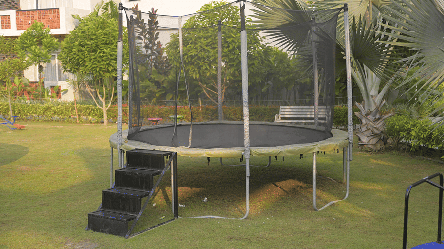 A children’s play area featuring an outdoor trampoline surrounded by plants and open lawn at Hotel Sonar Bangla, Mayapur.