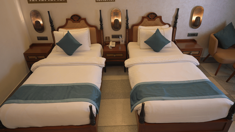 2 single beds with white linens, teal runners, and blue cushions in a guest room at Hotel Sonar Bangla, Mayapur.