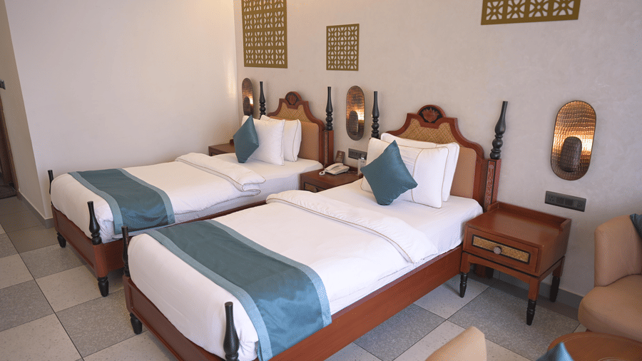 A guest room with 2 single beds featuring dark wood frames and blue runners at Hotel Sonar Bangla, Mayapur. 