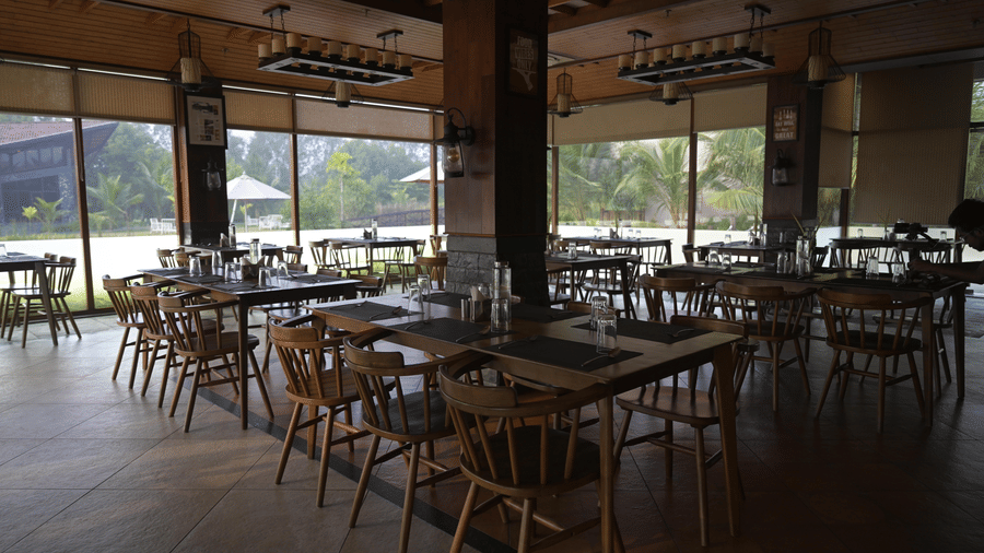 Restaurant at Hotel Sonar Bangla, Sundarban with wooden tables, chairs, lantern pendant lighting, and large windows.