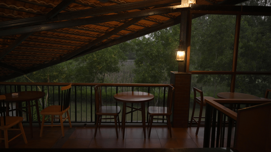 An outdoor wooden balcony area with tables and chairs overlooking trees at Hotel Sonar Bangla, Sundarban.