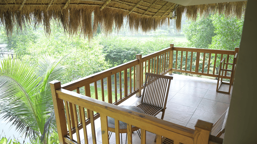 A balcony with a wooden railing under a thatched roof overlooking a tropical landscape at Hotel Sonar Bangla, Sundarban.