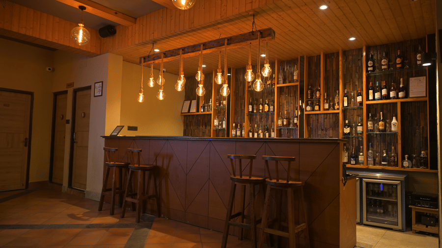 A wooden bar counter with high stools and hanging lights next to a doorway at Hotel Sonar Bangla, Sundarban.