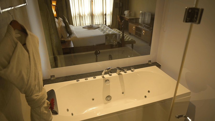  A white bathtub in a bathroom with a large mirror reflecting the bedroom at Hotel Sonar Bangla, Sundarban.