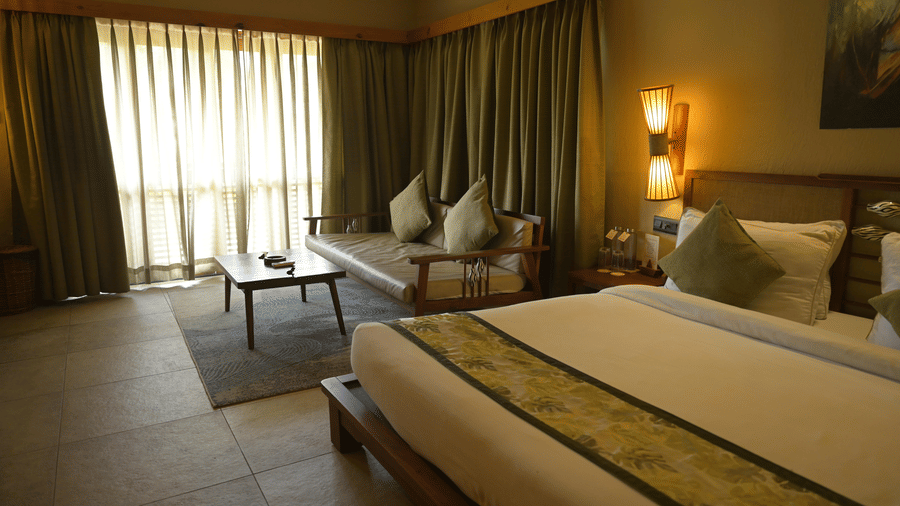 A hotel room featuring a bed,  a sofa area with a coffee table, and floor-to-ceiling curtains at Hotel Sonar Bangla, Sundarban.