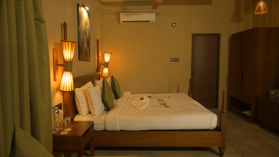 Wide view of a hotel room featuring a bed with white linens, wall lamps, and a wooden wardrobe at Hotel Sonar Bangla, Sundarban.