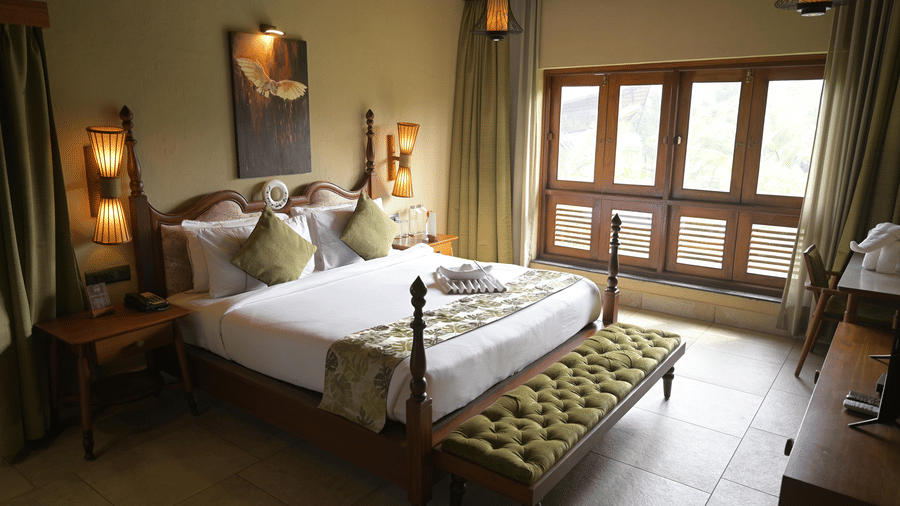 A bedroom featuring a large bed with white linens, green accents and large wooden-framed windows at Hotel Sonar Bangla, Sundarban.