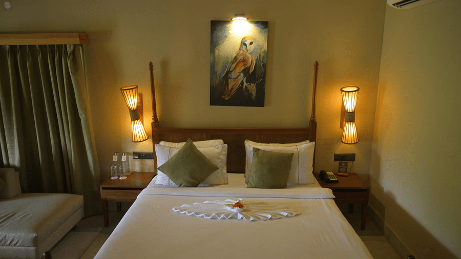 A double bedroom with a large bed, white linens, green pillows, and wall art at Hotel Sonar Bangla, Sundarban.