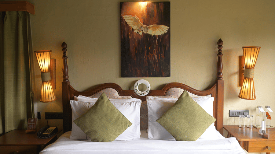 Close-up of a 4-poster bed with white linens, green pillows, and bedside lamps at Hotel Sonar Bangla, Sundarban.