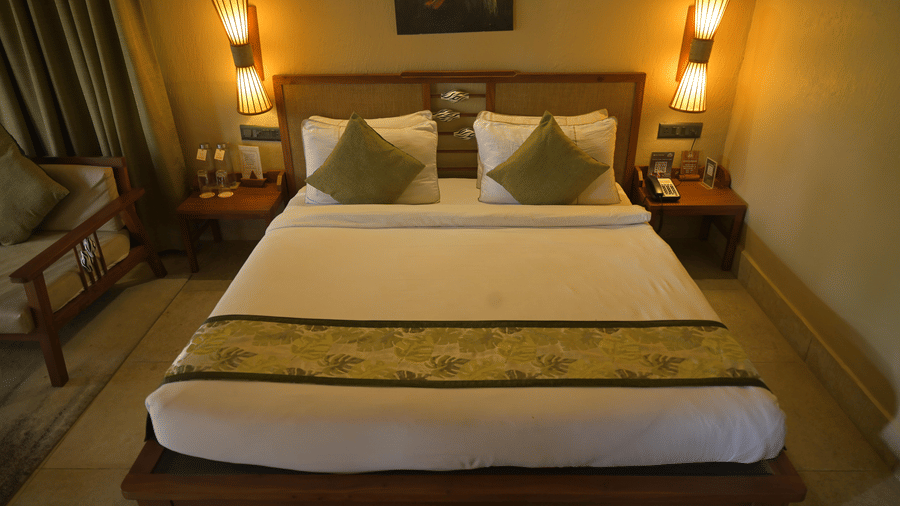 Front view of a made-up bed with white sheets and a green patterned bed runner at Hotel Sonar Bangla, Sundarban.