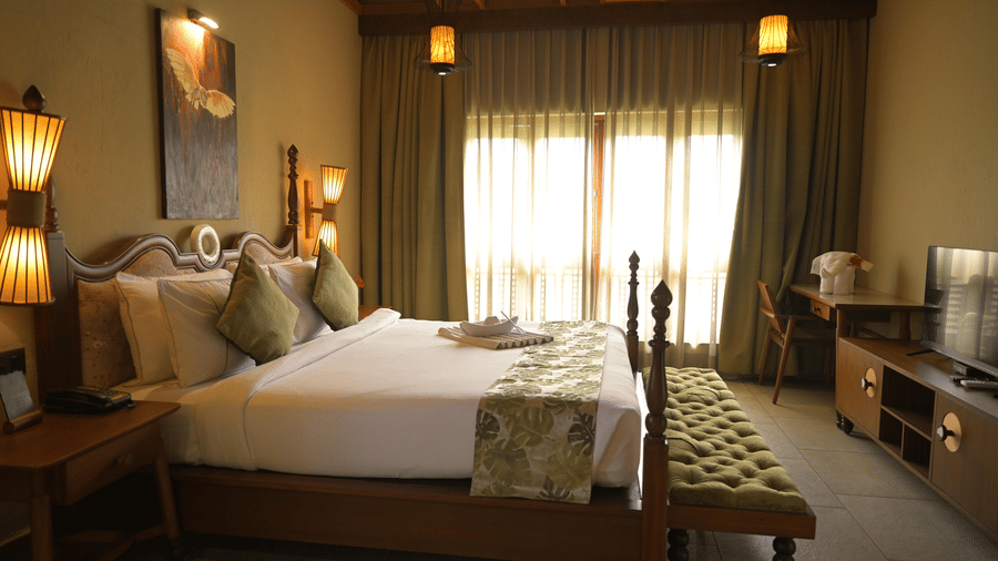 Full view of a hotel room with a wooden bed, television, and large windows with curtains at Hotel Sonar Bangla, Sundarban.