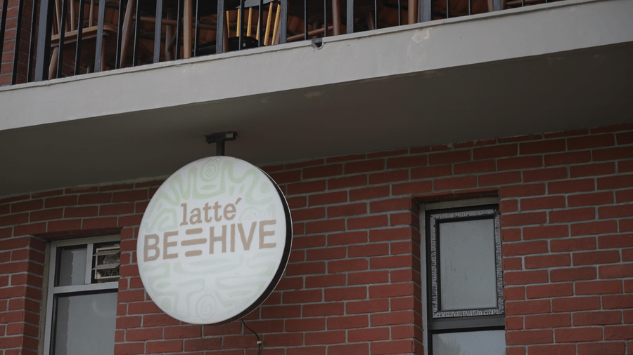 A circular white sign for Latte Beehive mounted on a red brick wall below a balcony at Hotel Sonar Bangla, Sundarban.