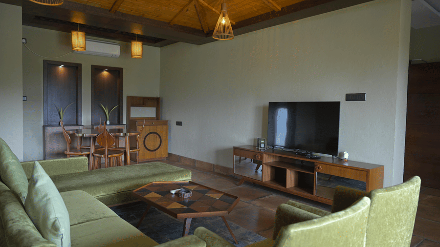 Living area featuring green velvet sofas, a wooden coffee table, and a television on a wooden stand at Hotel Sonar Bangla, Sundarban.