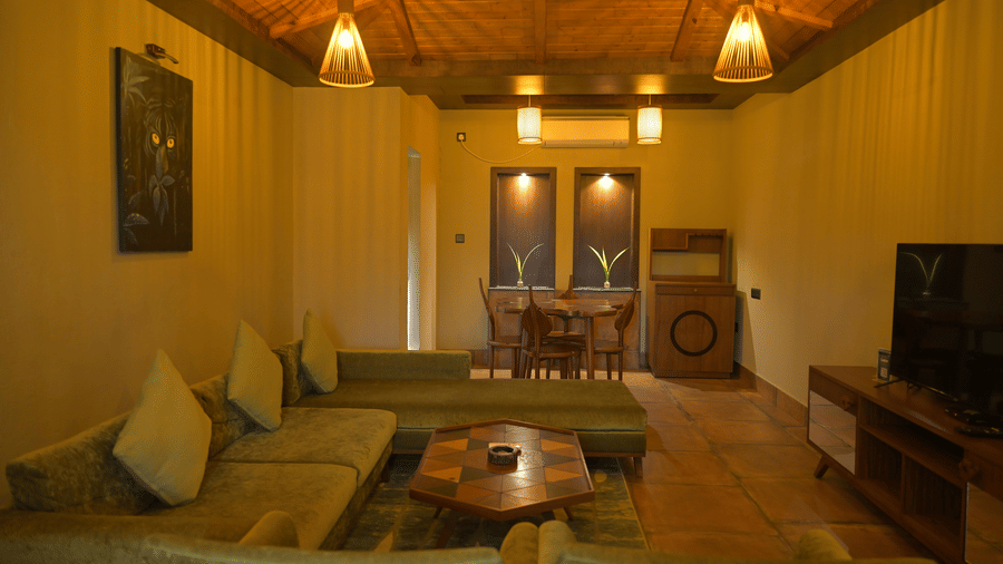 A seating area with a green L-shaped sofa and wooden dining table in the background at Hotel Sonar Bangla, Sundarban.