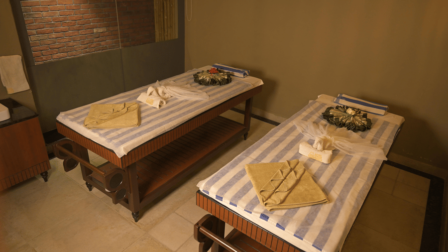 2 wooden massage tables side-by-side with striped towels and decorative items in a spa room at Hotel Sonar Bangla, Sundarban.