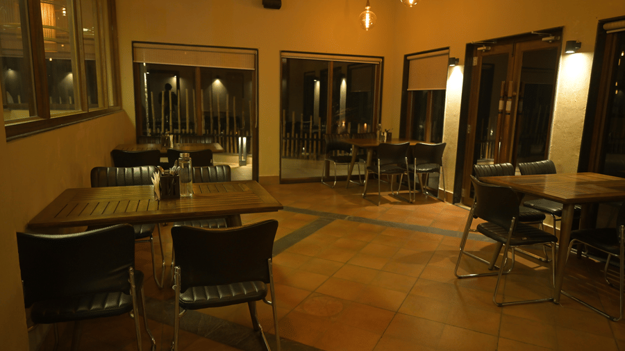 Interior view of a restaurant with wooden tables, chairs, and glass doors at Hotel Sonar Bangla, Sundarban.