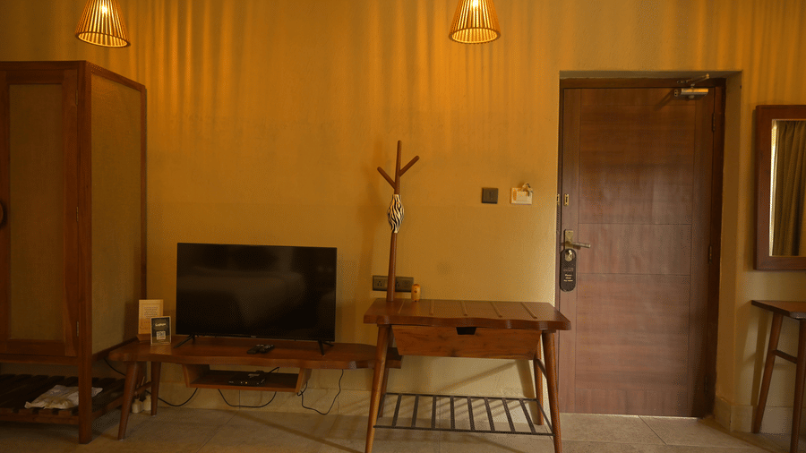 A television on a wooden bench next to a cupboard and wooden door at Hotel Sonar Bangla, Sundarban.