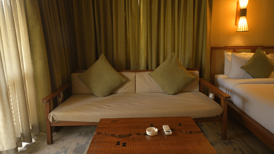 A wooden sofa with green cushions and a low coffee table in a room with curtains at Hotel Sonar Bangla, Sundarban.