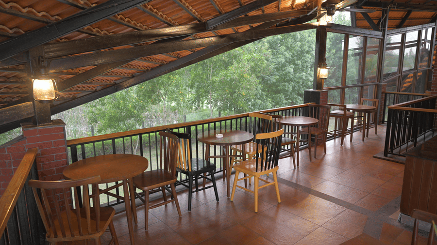  A wooden terrace with tables, chairs, and a railing under a pitched roof at Hotel Sonar Bangla, Sundarban.