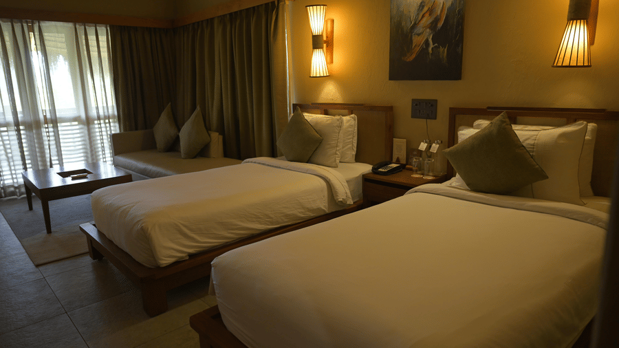 A twin bedroom with single beds, white linens, and wall-mounted lamps at Hotel Sonar Bangla, Sundarban. 