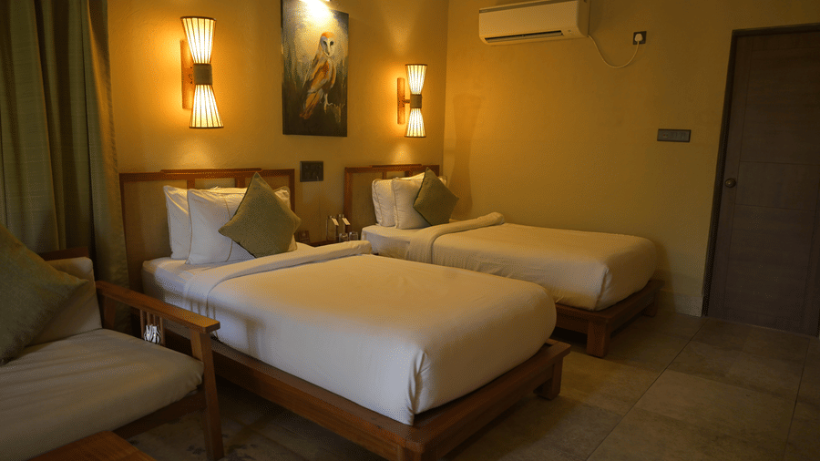 2 single beds with white linens and green pillows under wall-mounted lamps at Hotel Sonar Bangla, Sundarban.
